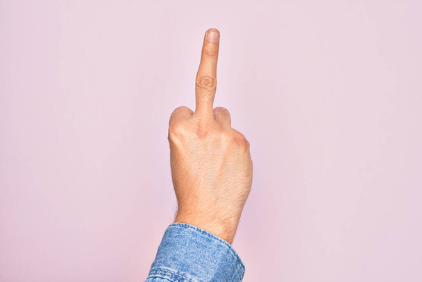 Hand of caucasian young man showing fingers over isolated pink background showing provocative and rude gesture doing fuck you symbol with middle finger - Photo, Image