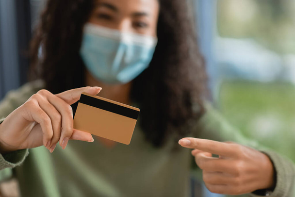 donna afroamericana in maschera medica che punta con il dito alla carta di credito - Foto, immagini