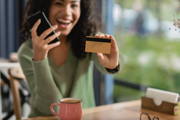 credit card and smartphone in hands of excited african american woman on blurred background  - Photo, Image