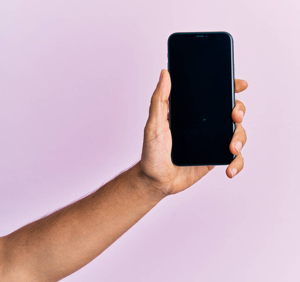 Hand of young hispanic man showing smartphone over isolated pink background. - Фото, изображение