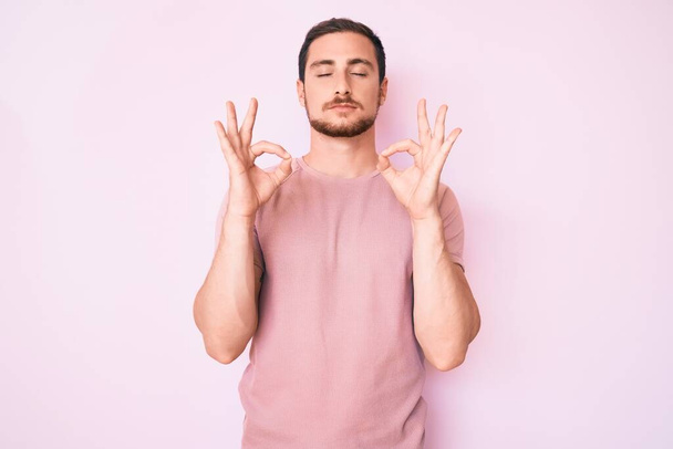 Jonge knappe man draagt casual tshirt ontspannen en glimlachen met de ogen dicht doen meditatie gebaar met de vingers. yoga concept.  - Foto, afbeelding