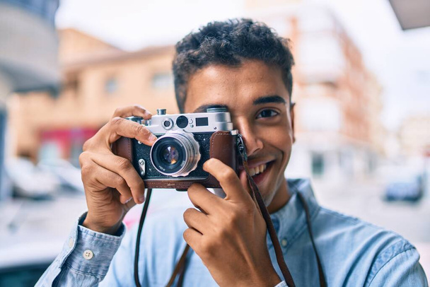 Fiatal latin turista férfi mosolyog boldog segítségével vintage kamera séta a városban. - Fotó, kép