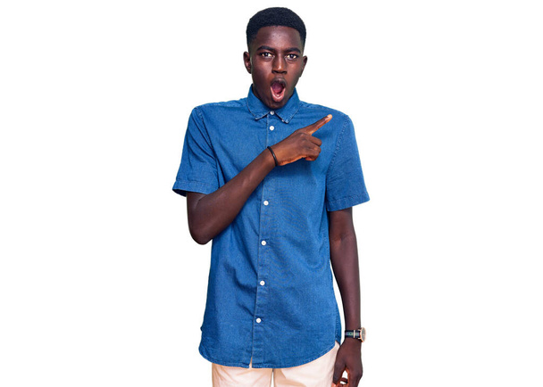 Young african american man wearing casual clothes surprised pointing with finger to the side, open mouth amazed expression.  - 写真・画像