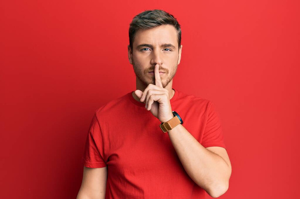 Handsome caucasian man wearing casual red tshirt asking to be quiet with finger on lips. silence and secret concept.  - Photo, Image