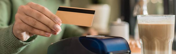 vidro de latte perto de cartão de crédito na mão de mulher afro-americana pagando em fundo borrado, banner - Foto, Imagem