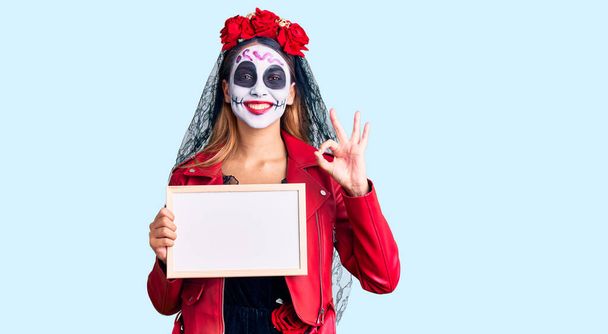 Woman wearing day of the dead costume holding empty white chalkboard doing ok sign with fingers, smiling friendly gesturing excellent symbol  - Photo, Image
