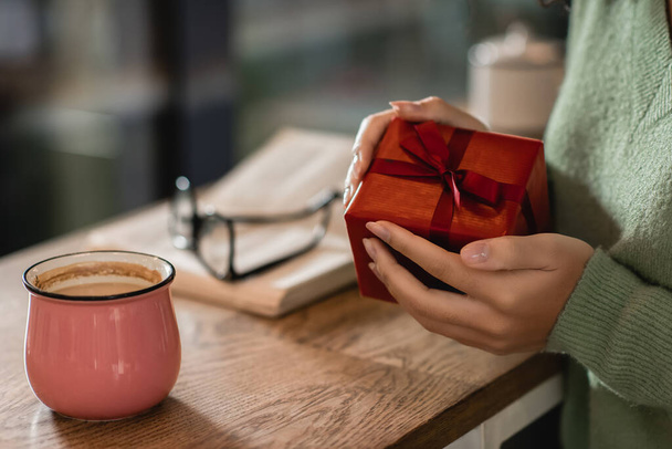 cropped view of african american woman holding wrapped christmas present in cafe - Фото, изображение