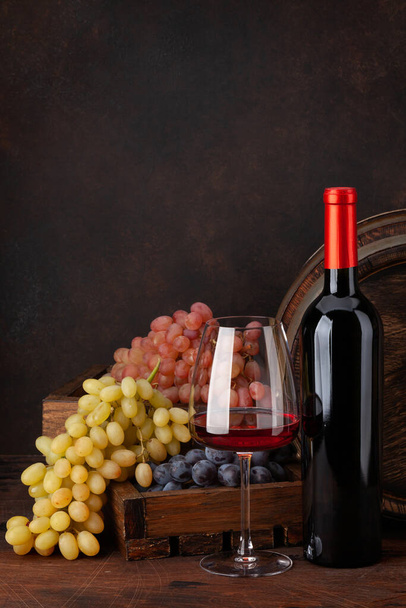 Бутылка вина, виноград, бокал красного вина и старая деревянная бочка. С копировальным местом - Фото, изображение