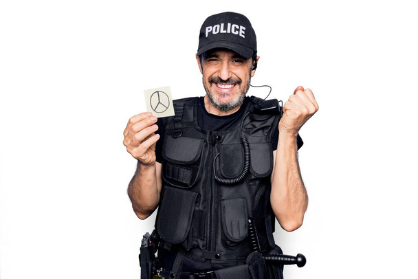 Полицейский средних лет в полицейской форме держит напоминание бумагу с символом мира кричит гордо, празднует победу и успех очень взволнован с поднятой рукой - Фото, изображение