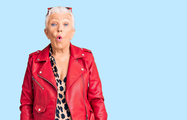 Senior beautiful woman with blue eyes and grey hair wearing a modern style with a red leather jacket scared and amazed with open mouth for surprise, disbelief face  - Fotoğraf, Görsel