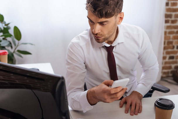 Üzletember használ okostelefon és számítógép, miközben ellenőrzi tanfolyamok irodai  - Fotó, kép