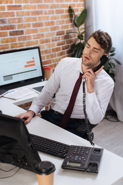 Бізнесмен розмовляє по телефону біля комп'ютерів і кави, щоб піти на розмитий передній план в офісі
  - Фото, зображення