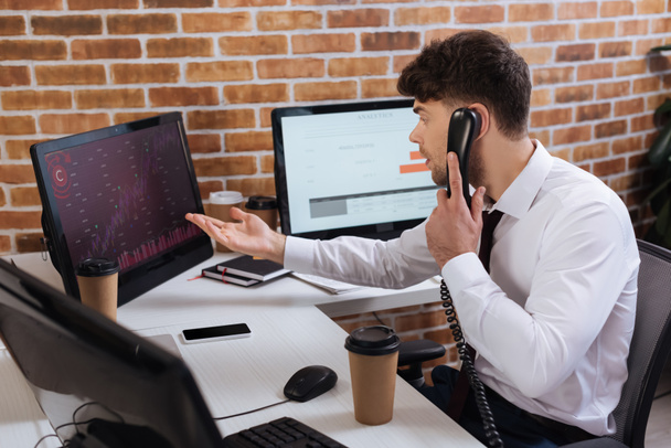 homme d'affaires parlant au téléphone et pointant vers l'ordinateur avec des graphiques des cours financiers  - Photo, image