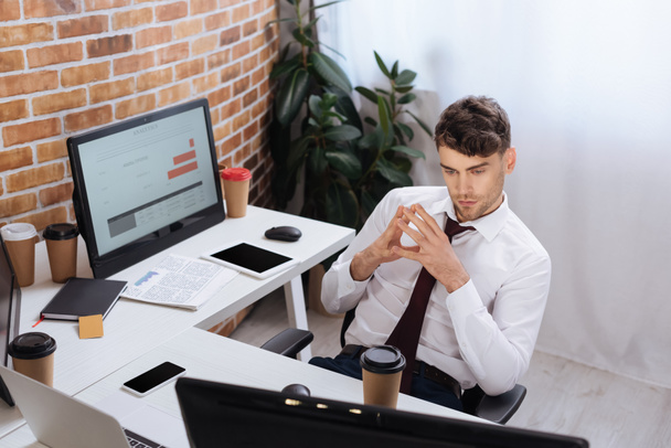 Fiatal üzletember néz számítógép monitor közel kávé menni, és szerkentyű az irodában  - Fotó, kép