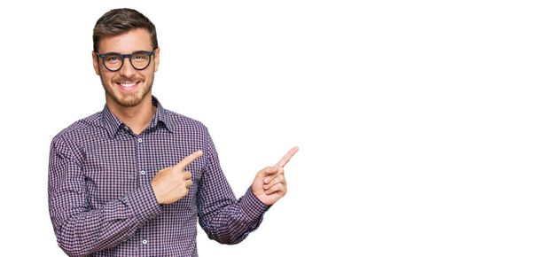 Handsome caucasian man wearing casual clothes and glasses smiling and looking at the camera pointing with two hands and fingers to the side.  - Photo, Image