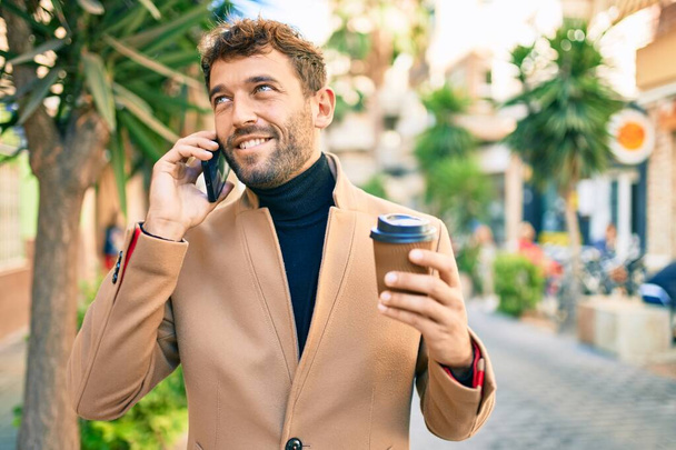 Komea liikemies yllään tyylikäs takki älypuhelimella hymyillen onnellinen ulkona - Valokuva, kuva