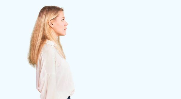 Jonge mooie blonde vrouw dragen casual shirt op zoek naar kant, ontspannen profiel poseren met natuurlijke gezicht met zelfverzekerde glimlach.  - Foto, afbeelding