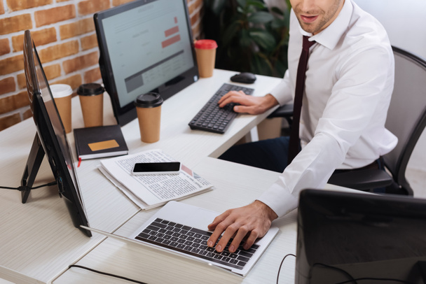 Vágott kilátás üzletember használja laptop és a számítógép, miközben ellenőrzi a pénzügyi készletek közelében okostelefon és hírek az irodában  - Fotó, kép