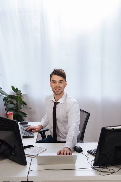 Smiling businessman using computers while checking finance market in office  - Φωτογραφία, εικόνα