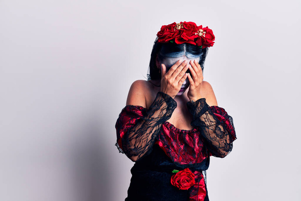 Junge Frau trägt mexikanischen Tag der Toten Make-up mit traurigem Gesichtsausdruck bedeckt Gesicht mit Händen beim Weinen. Depressionskonzept.  - Foto, Bild