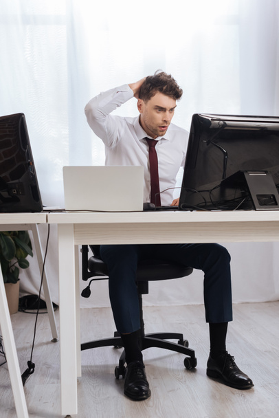 Беспокойный бизнесмен смотрит на компьютер во время проверки финансовых курсов в офисе  - Фото, изображение