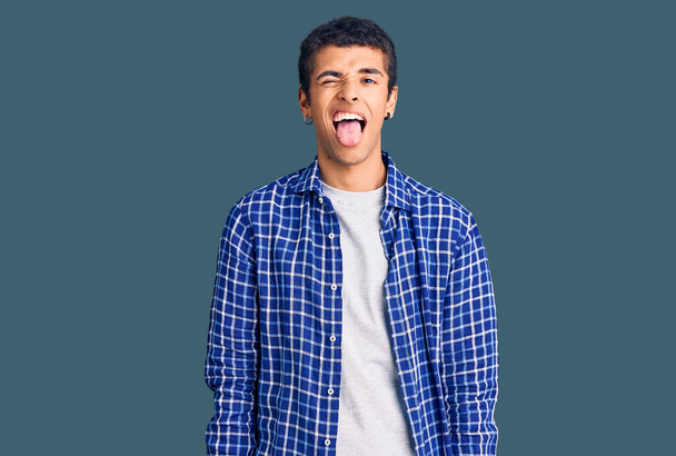 Genç Afro-Amerikan bir adam günlük giysiler giyiyor. Dilini komik bir ifadeyle dışarı çıkarıyor. duygu kavramı.  - Fotoğraf, Görsel