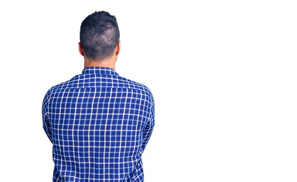 Junger hispanischer Mann in lässiger Kleidung steht rückwärts und blickt mit verschränkten Armen weg  - Foto, Bild