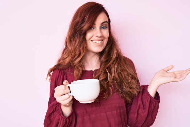 Junge schöne Frau hält Kaffee und feiert Leistung mit glücklichem Lächeln und Siegerausdruck mit erhobener Hand  - Foto, Bild