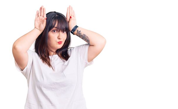 Young plus size woman wearing casual clothes doing bunny ears gesture with hands palms looking cynical and skeptical. easter rabbit concept.  - Photo, Image