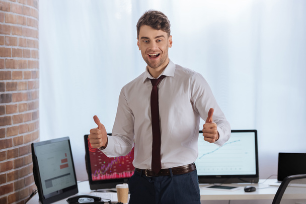 Веселый бизнесмен показывает, как жест с компьютерами на размытом фоне  - Фото, изображение