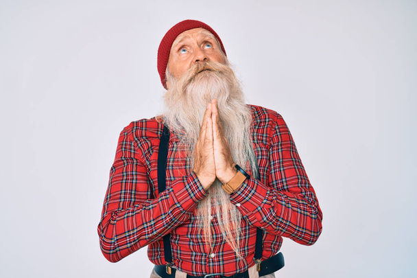 Oude senior man met grijs haar en lange baard dragen hipster look met wollen pet bedelen en bidden met de handen samen met hoop uitdrukking op het gezicht zeer emotioneel en bezorgd. bedelen.  - Foto, afbeelding