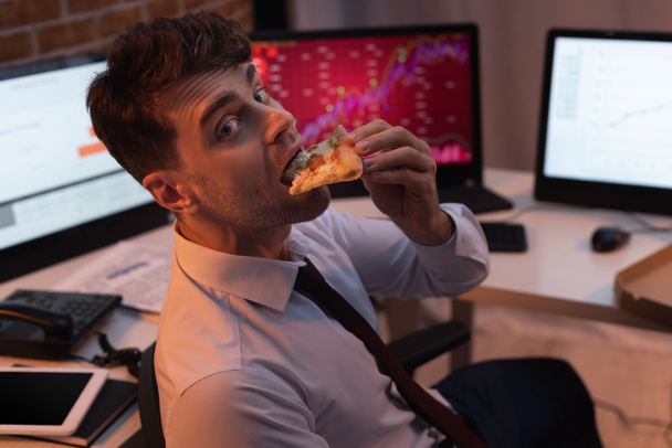 Empresario mirando la cámara mientras come pizza en la oficina por la noche  - Foto, Imagen