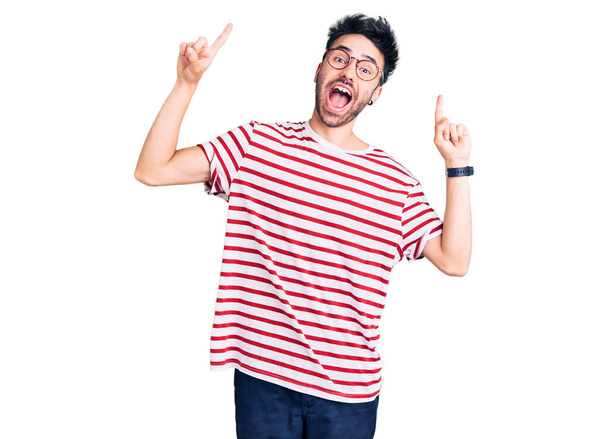 Young hispanic man wearing casual clothes smiling amazed and surprised and pointing up with fingers and raised arms.  - Foto, imagen
