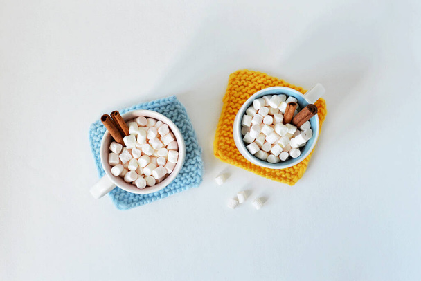 Mustard yellow and light blue handmade knitted coasters, cups with marshmallows and cinnamon over white - Fotó, kép