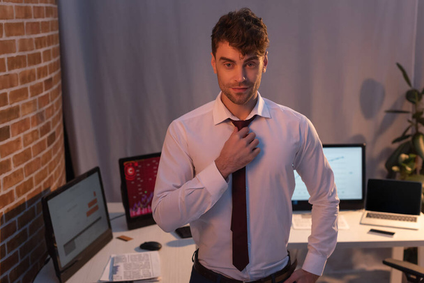 businessman looking at camera near computers in office in evening  - Photo, Image