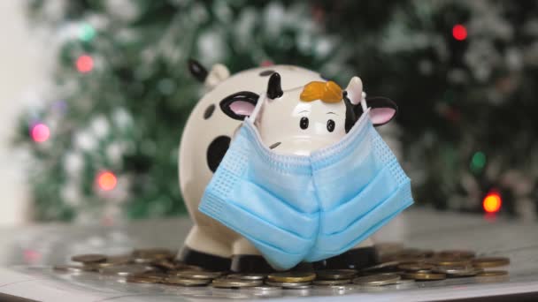 Figura de alcancía en forma de vaca o toro en una máscara médica. El impacto de la pandemia en la economía. Manos con un cerdito de cerca - Metraje, vídeo