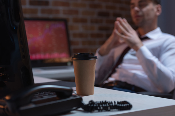 Koffie in de buurt van telefoon, computers en zakenman op wazige achtergrond - Foto, afbeelding