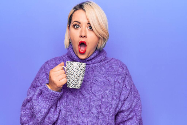 Young beautiful blonde plus size woman drinking mug of hot coffee over purple background scared and amazed with open mouth for surprise, disbelief face - Photo, Image