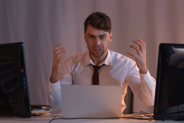 Aggressive businessman looking at camera near computers on blurred foreground  - Photo, Image