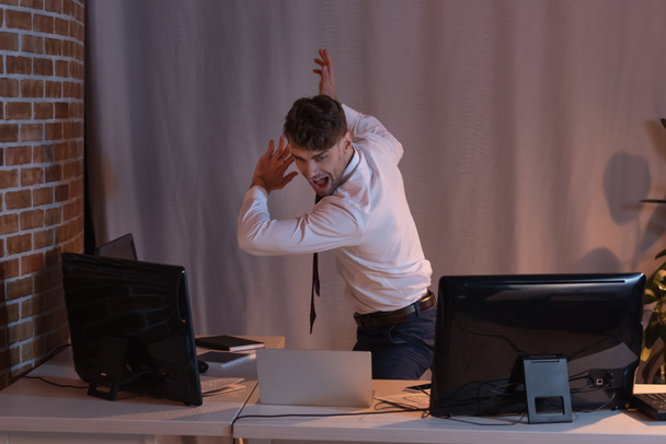 Schreeuwende zakenman in de buurt van computers in het kantoor tijdens de avond  - Foto, afbeelding