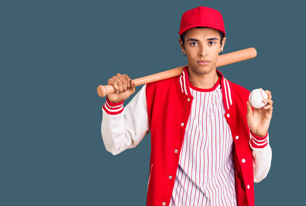 Jeune homme afro-américain jouant au baseball tenant chauve-souris et balle pensée attitude et expression sobre regardant confiant en soi  - Photo, image