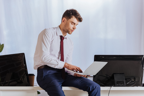 Junger Geschäftsmann nutzt Laptop in der Nähe von Computern und Kaffee, um ins Büro zu gehen  - Foto, Bild