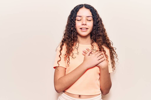 Beautiful kid girl with curly hair wearing casual clothes smiling with hands on chest with closed eyes and grateful gesture on face. health concept.  - Photo, Image