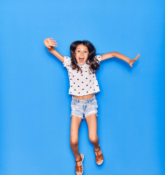 Adorable hispanic child girl wearing casual clothes smiling happy. Jumping with smile on face over isolated blue background - Photo, Image