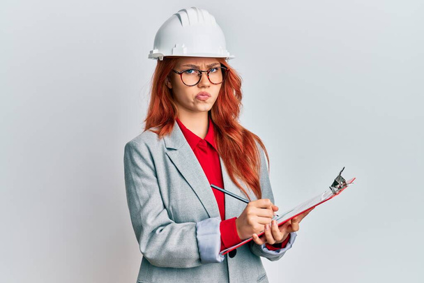 Young redhead woman wearing architect hardhat skeptic and nervous, frowning upset because of problem. negative person.  - Photo, Image