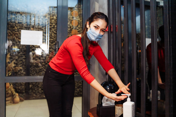 アルコール防腐ゲルを使用して保護マスクを身に着けている女性は、カフェでコロナウイルスCovid-19の発生を防ぐ.消毒は公共の場所を訪れる上で重要な部分です。. - 写真・画像