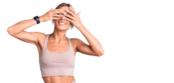 Beautiful caucasian woman wearing sportswear covering eyes with hands smiling cheerful and funny. blind concept.  - Photo, Image