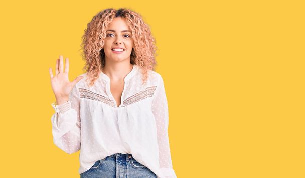 Young blonde woman with curly hair wearing elegant summer shirt showing and pointing up with fingers number five while smiling confident and happy.  - Photo, Image