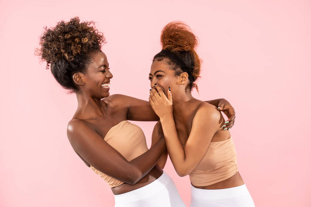 Studio shot of happy Afro female sisters enjoying good moment, chatting and having fun together during free time, isolated over pink pastel studio background. Friendship and real people emotions concept. - Φωτογραφία, εικόνα