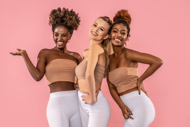 Group of happy young women standing together on pink pastel studio background. Multi ethnic female friends smiling to the camera. Fit bodies. Healthy lifestyle and friendship concept. - Photo, Image